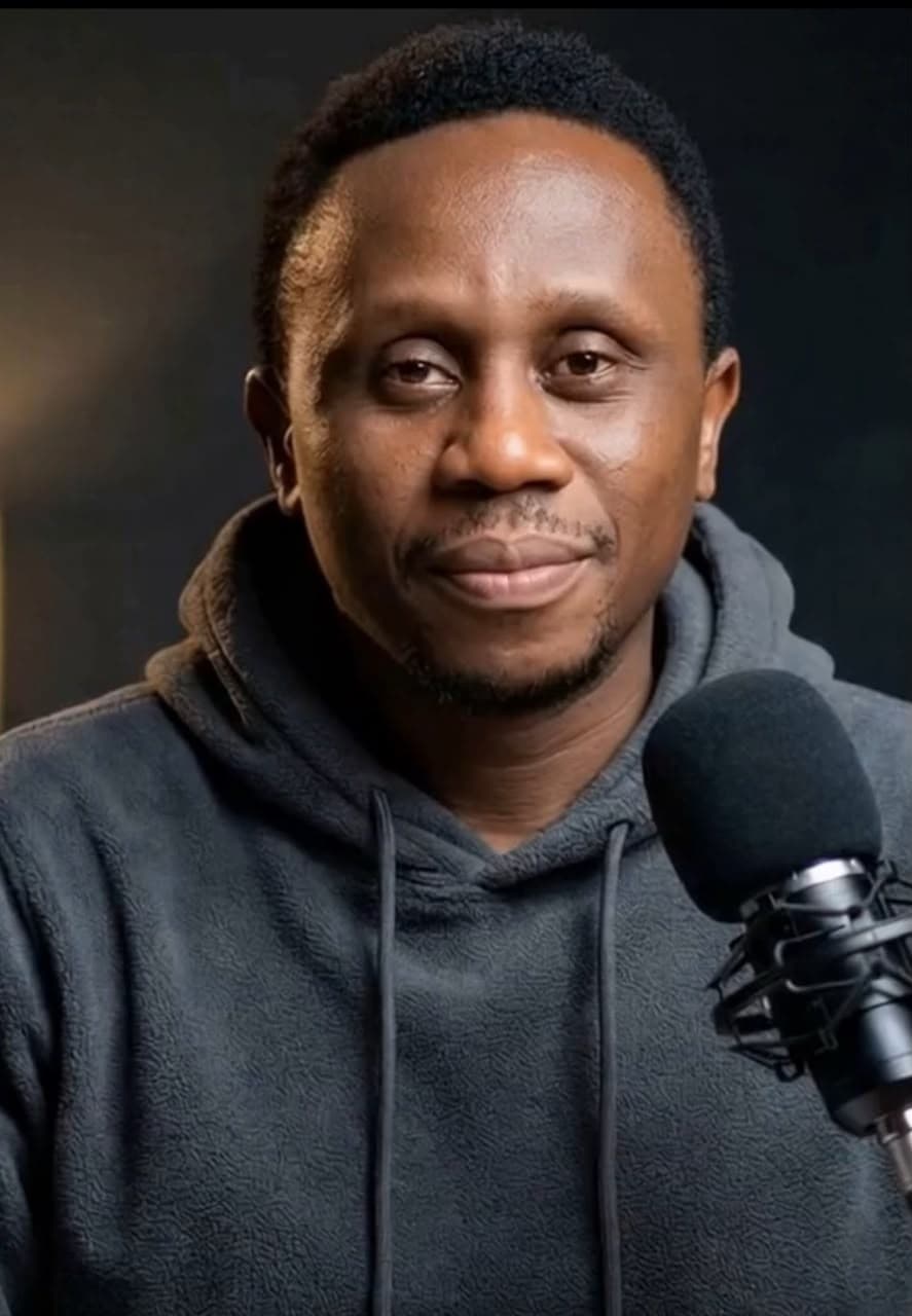 Daniel Makonor, AI Skill Educator at AIMoniPoint, smiling in a grey hoodie beside a podcast microphone